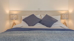Una cama bien tendida con dos almohadas, dos lámparas de noche con pantallas estampadas y un cabecero de madera.