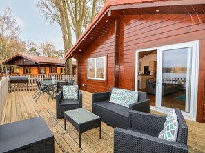 A wooden cabin with a deck, furnished with wicker furniture and a grill. - Teal Lodge (Lincoln)