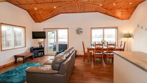 A spacious living area with a wooden ceiling, a sofa, a dining table with chairs, and a TV mounted on the wall. - Teal Lodge (Lincoln)