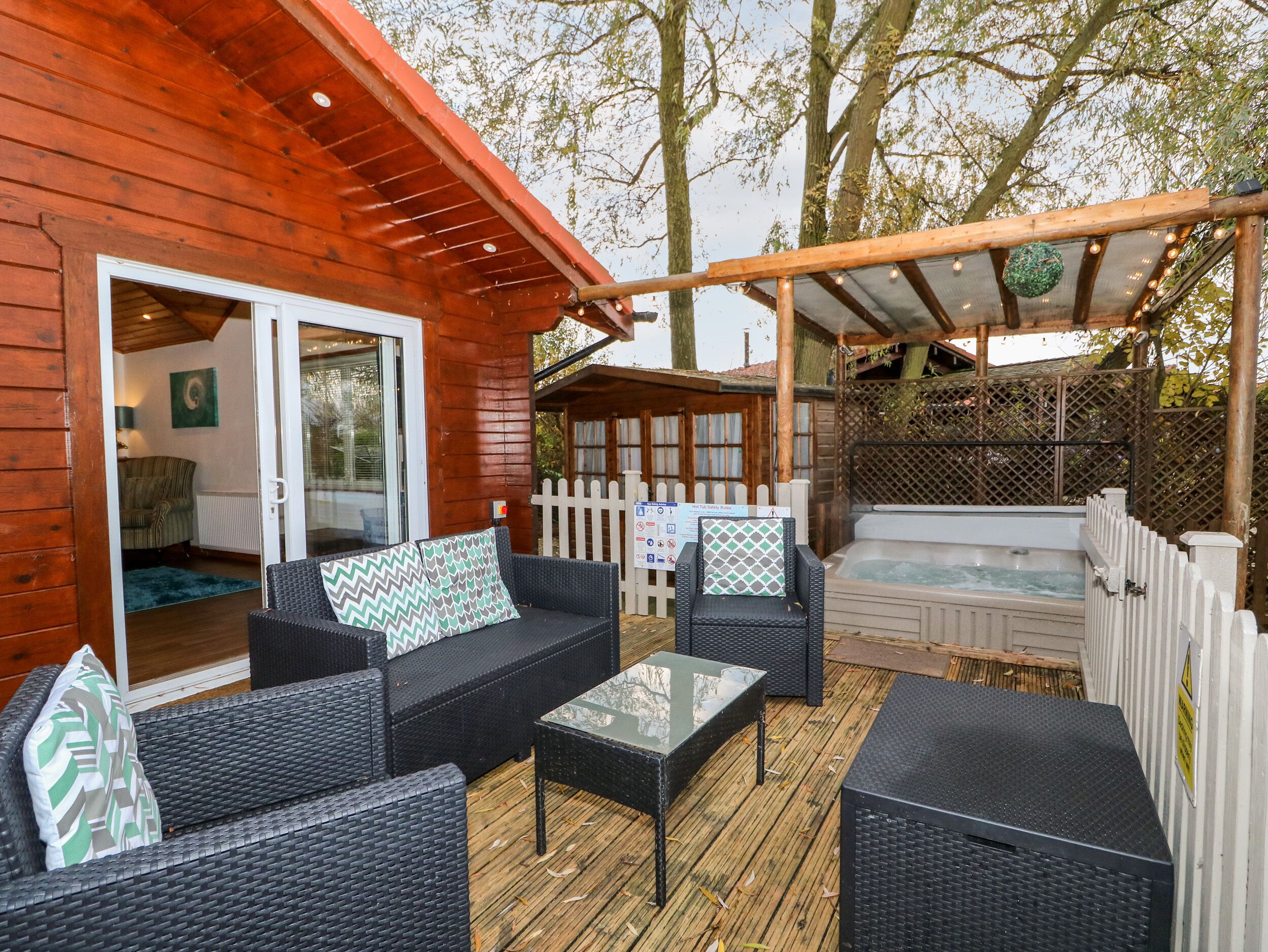 Una terraza de madera con mobiliario exterior, un jacuzzi y una zona cubierta con luces colgantes.