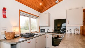 A modern kitchen with white cabinets, a microwave, a toaster, a kettle, and a stove. There is a window with a view of trees outside. - Teal Lodge (Lincoln)