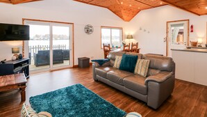 A cozy living room with a wooden ceiling, a leather sofa, a blue rug, and a television on a wooden table. - Teal Lodge (Lincoln)