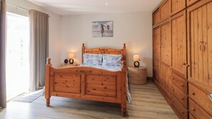 A bedroom with a wooden bed, two bedside tables with lamps, a large wooden wardrobe, and a painting on the wall. - Seashells (Coleraine)