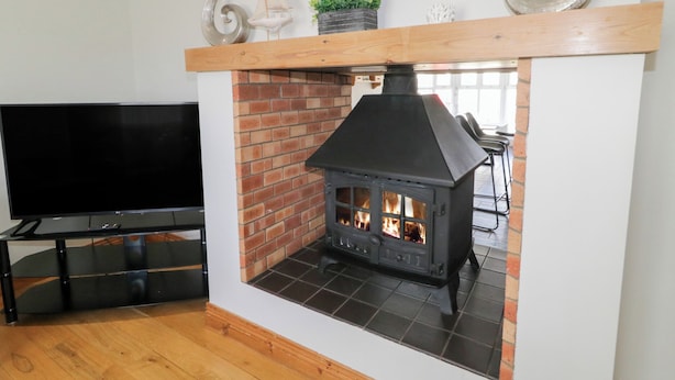 A living room with a fireplace, a TV, and a wooden shelf above the fireplace. - Seashells (Coleraine)