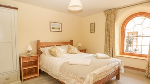 Une chambre à coucher bien rangée, avec un lit, des tables de chevet, une armoire et une fenêtre avec des rideaux.