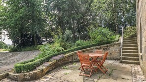 Un espace extérieur aménagé avec une allée pavée, un escalier en pierre, une table avec des chaises et une végétation luxuriante.