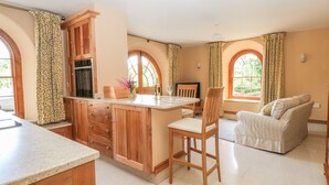 Une cuisine spacieuse avec des meubles de rangement en bois, un coin repas avec un canapé et de grandes fenêtres dotées de rideaux.