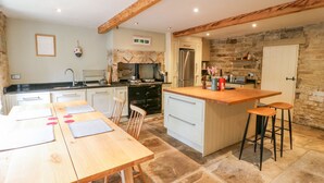 A kitchen with a central island, white cabinets, and a stone wall. - Bamforth Cottage (Holmfirth)