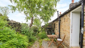 A rustic garden with a wooden deck, a stone wall, and a brick building. - Bamforth Cottage (Holmfirth)
