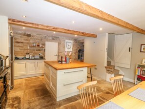 A kitchen with white cabinets, a wooden countertop, and a stone wall. There is a sink, a stove, and a chair. - Bamforth Cottage (Holmfirth)