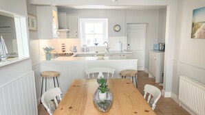 Eine moderne Küche mit weißen Schränken, einer zentralen Kochinsel und einem Essbereich mit Holztisch und weißen Stühlen.