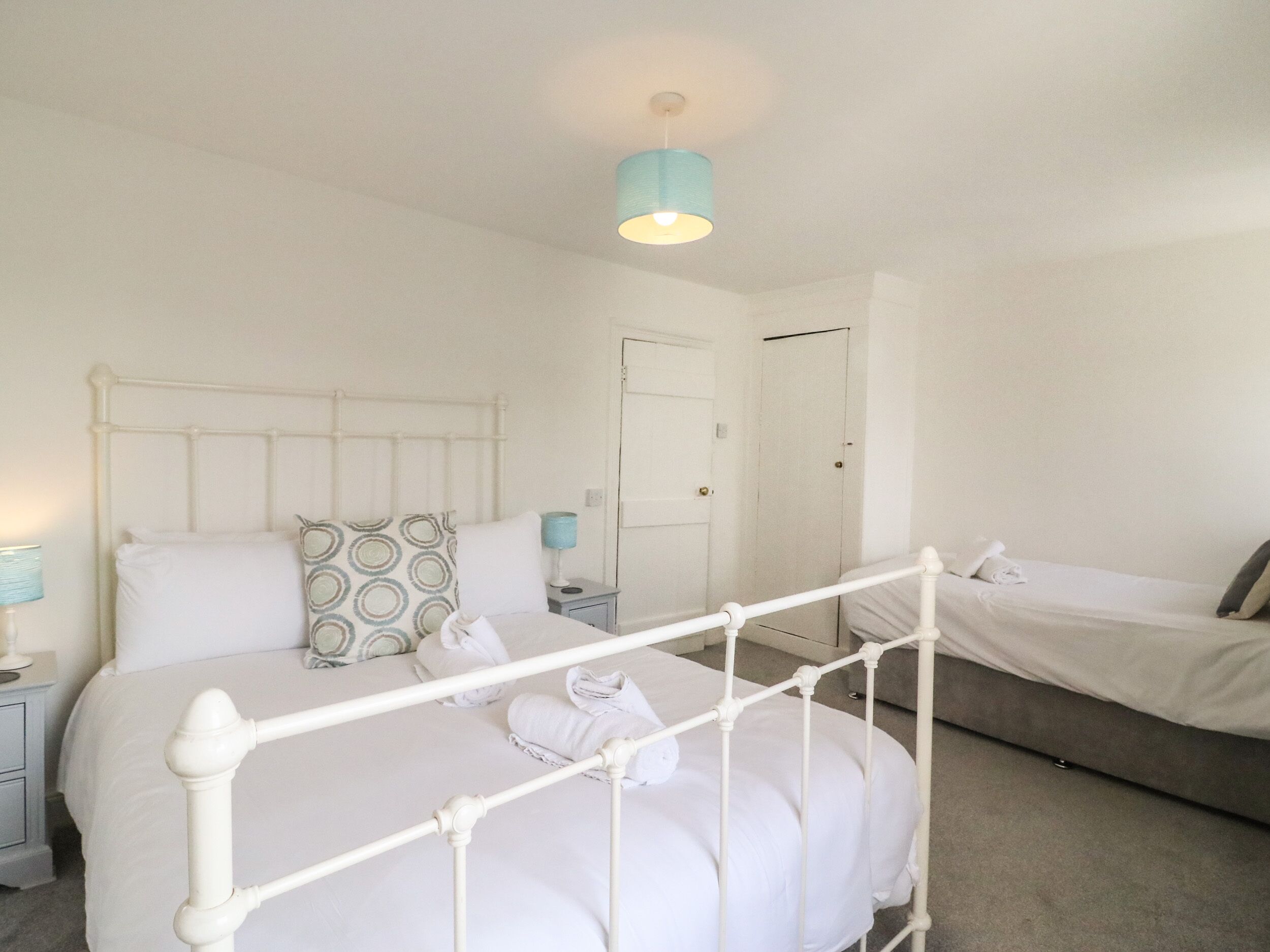 A bedroom with a white metal bed frame, a bedside table with a lamp, a door, and a small window.