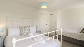 A bedroom with a white metal bed frame, a bedside table with a lamp, a door, and a small window.