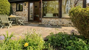 A stone building with a patio, outdoor seating, and a garden with various plants and flowers. - Puffin Cottage (Axminster)
