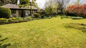 A well-maintained garden with a stone house, a lawn, and various plants and trees. - Puffin Cottage (Axminster)