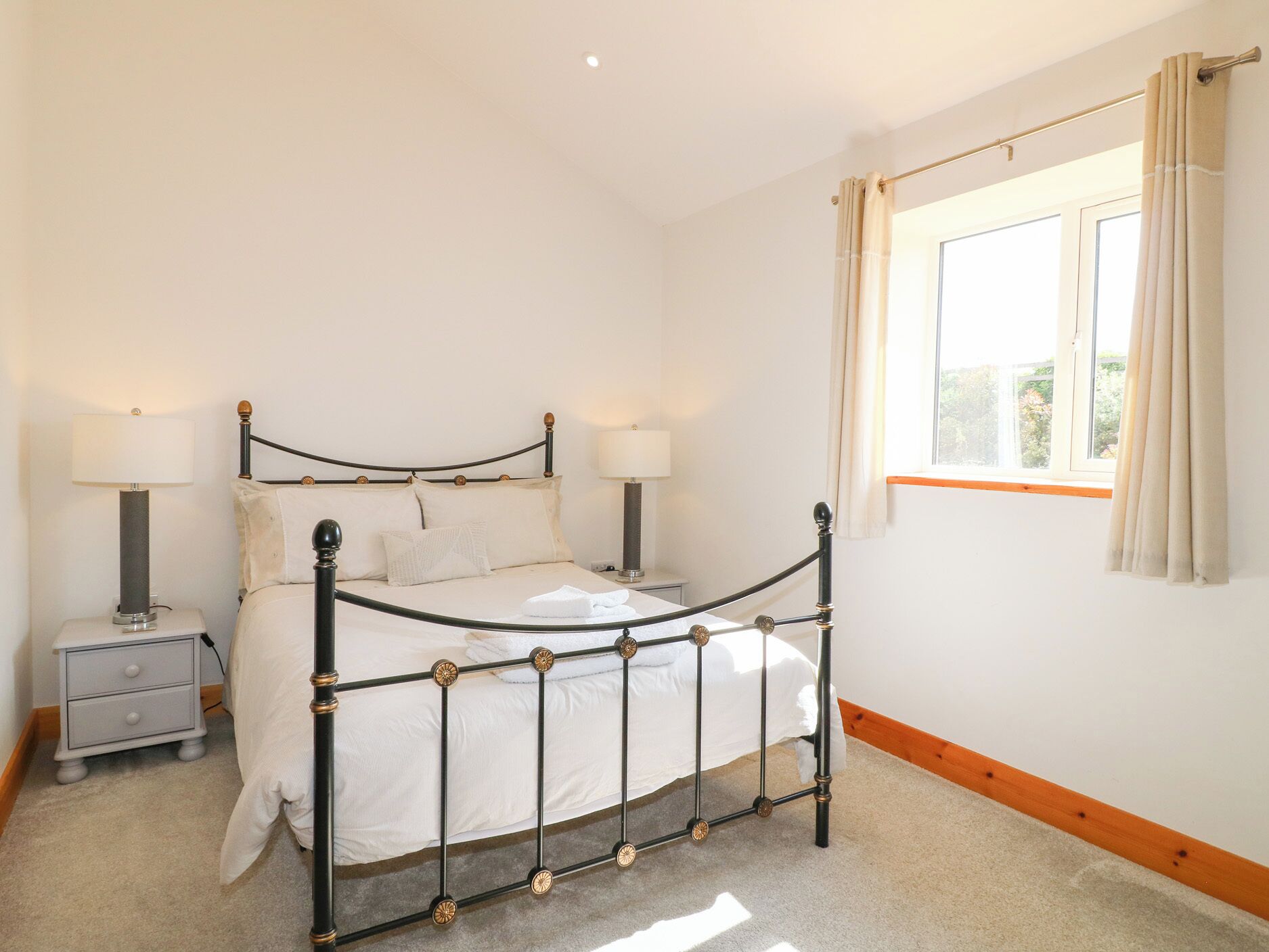 A neatly arranged bedroom with a bed, bedside tables, and a window with curtains.