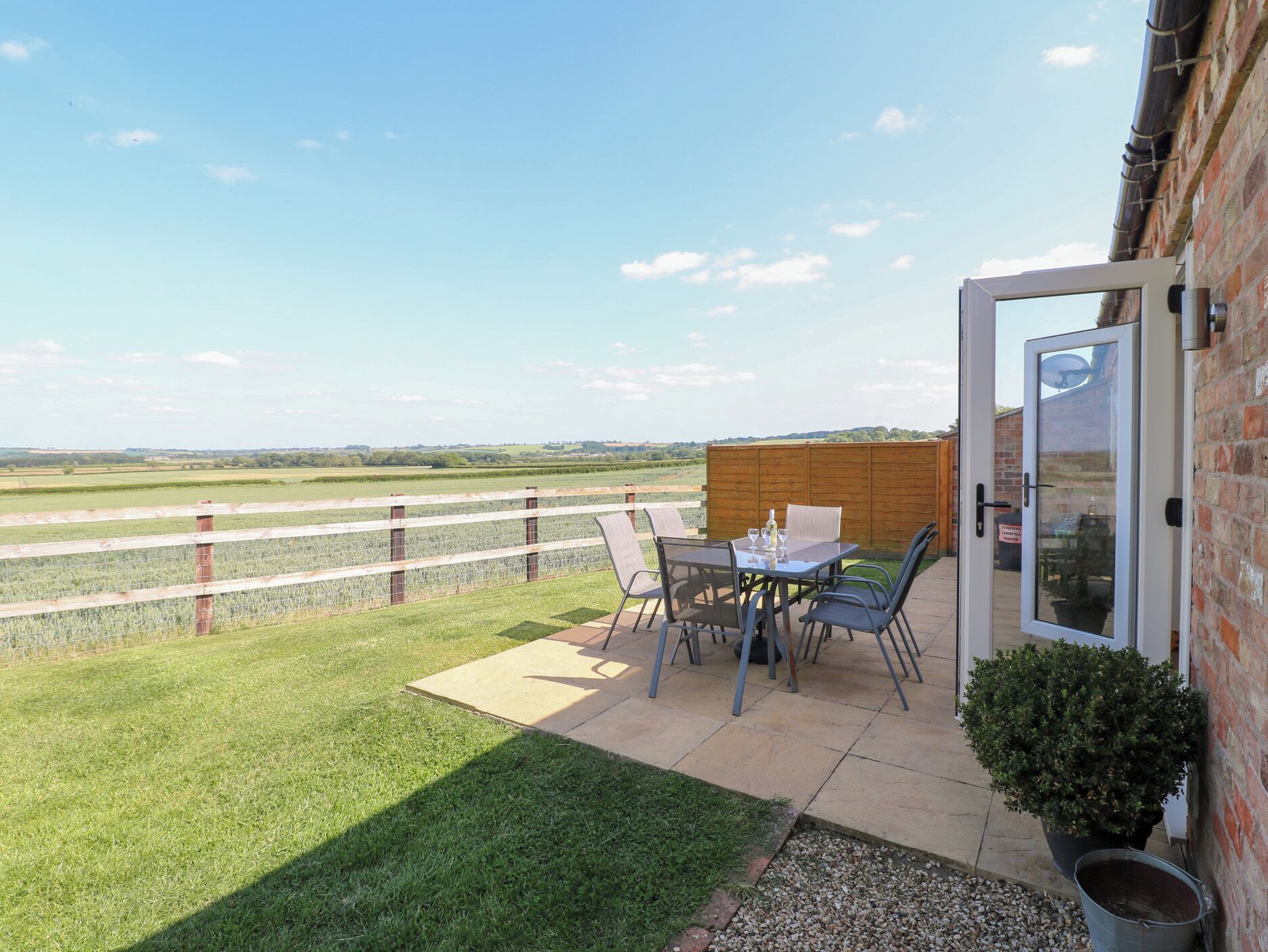 Eine Terrasse mit Tisch und Stühlen, einem Blumentopf und Blick auf ein Feld.