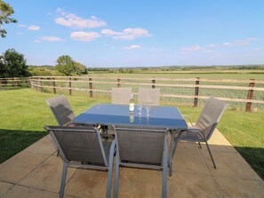 An outdoor patio with a table and four chairs, surrounded by a wooden fence and a view of a green field. - Mandarin Cottage (Melton Mowbray)