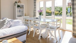 Un salon lumineux comprenant un canapé, une table à manger avec des chaises, une bibliothèque et une grande porte-fenêtre coulissante donnant sur un jardin.