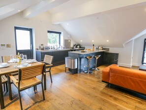 A modern kitchen with a central island, a dining area with a wooden table and chairs, and an orange sofa in a loft-style living space. - Lake View (Windermere)