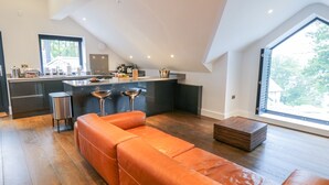 A modern kitchen with a central island, a dining area with orange leather seating, and a large window offering a view of the outdoors. - Lake View (Windermere)