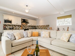 Ein modernes Wohnzimmer mit einem beigefarbenen Ecksofa, einem Holztisch und einer Weinflasche.