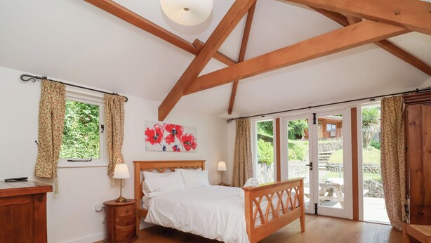 Une chambre à coucher avec un lit en bois, une table de chevet, une commode et une grande fenêtre avec des rideaux.