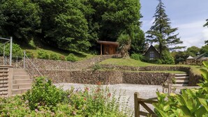 Un jardin avec un mur de pierre, des marches en bois et un petit bâtiment en bois.
