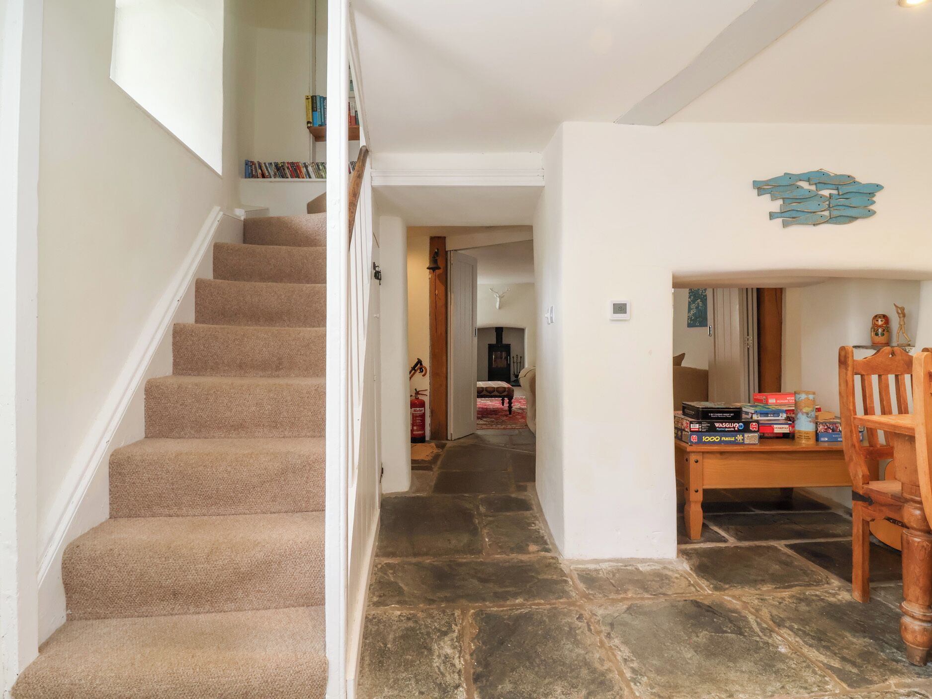 A staircase leading to a living area with a stone floor, a fireplace, and a dining table with books and puzzles.