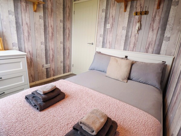 Un dormitorio con pared de madera, una cama con ropa de cama gris, un tocador blanco y una alfombra rosa.