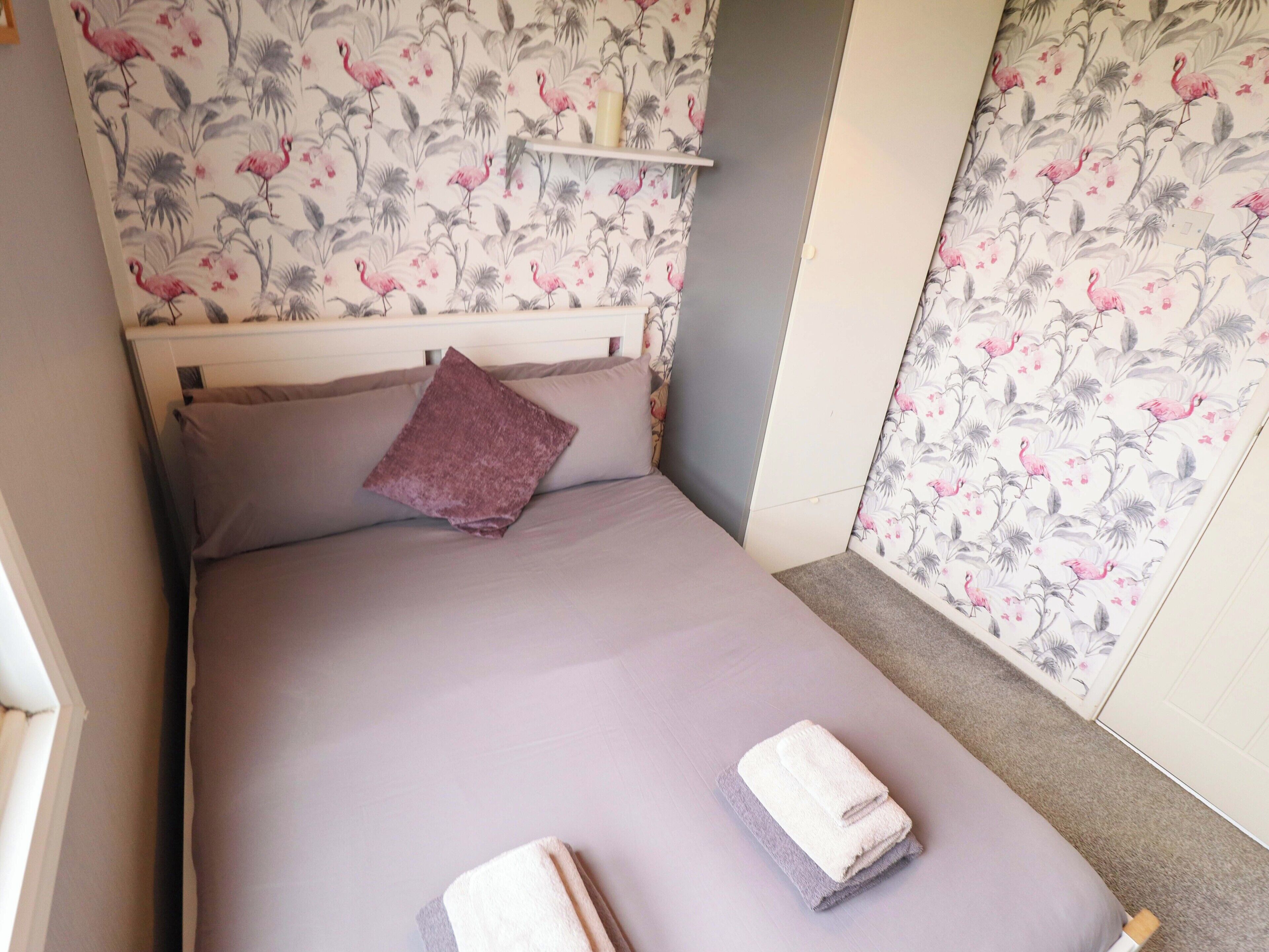 A small, neatly made bed with a purple pillow and two folded towels.