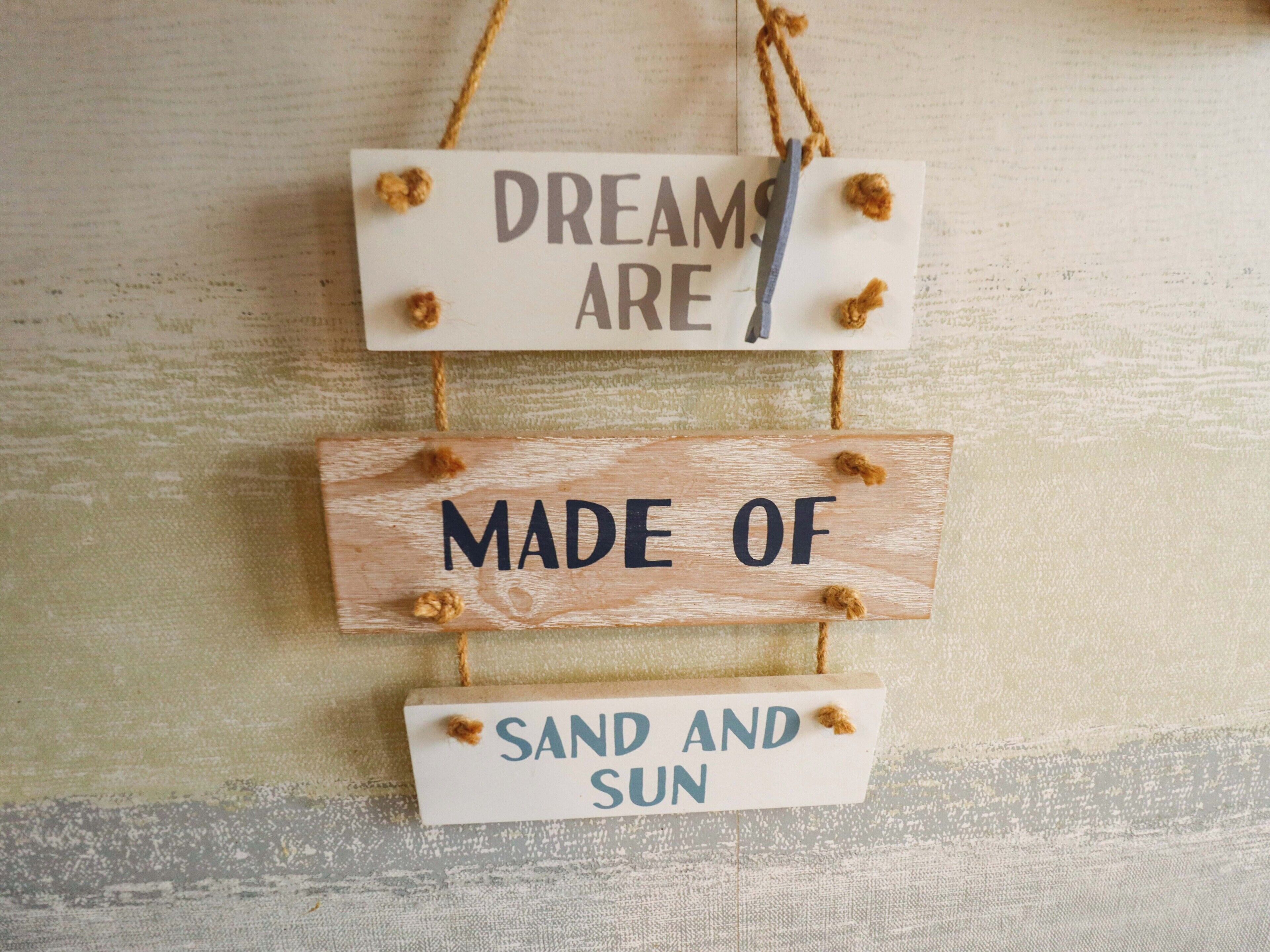 A wooden sign with the text 'DREAMS ARE MADE OF SAND AND SUN' hanging on a textured wall.