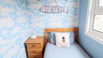 Une chambre avec un lit, une table de chevet, une commode en bois, un mur orné d’un motif de nuages et un panneau indiquant « PLAGE ».
