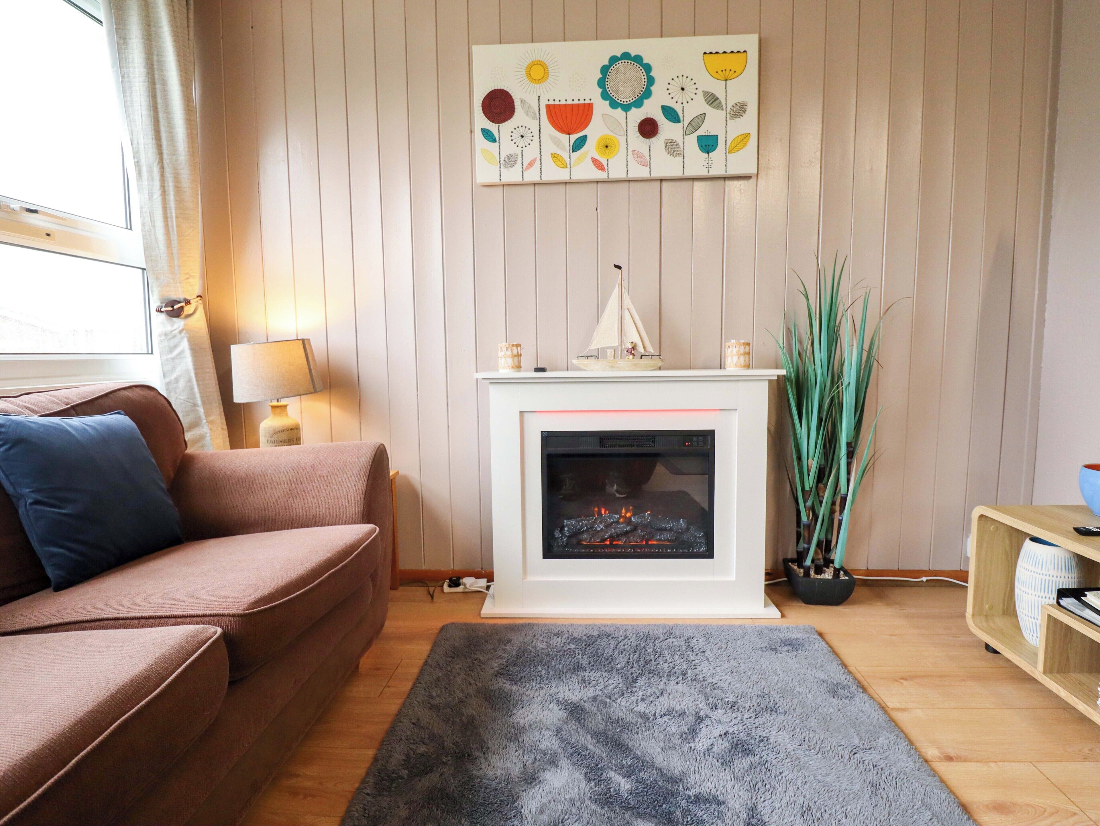 A living room with a sofa, a fireplace, a rug, and a wall-mounted artwork.