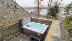 Área de banheira de pedra com degraus que levam a uma piscina, cercada por árvores e vista para um lago.