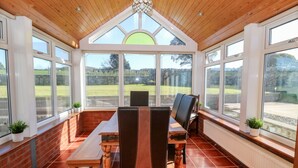A covered patio with a wooden ceiling, large windows, and a view of a grassy area. - Buarthau Cottage (Caernarfon)