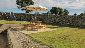 A wooden picnic table with a canopy, surrounded by a stone wall and a grassy lawn. - Buarthau Cottage (Caernarfon)
