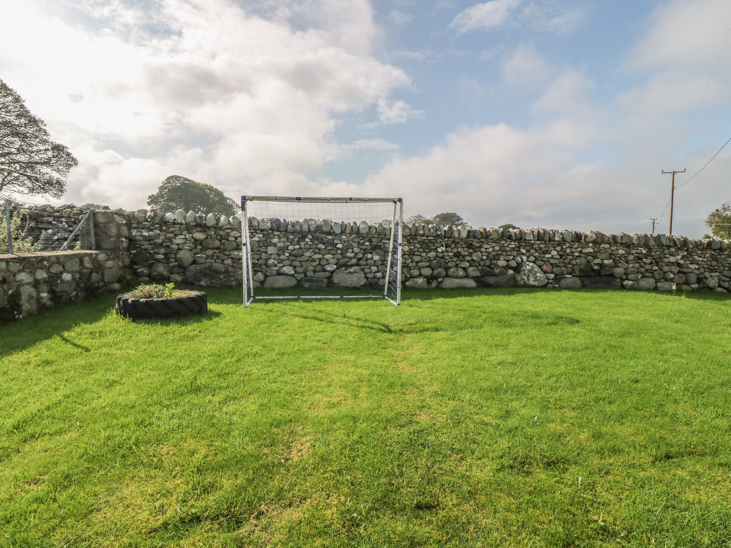A grassy field with a stone wall and a goalpost.