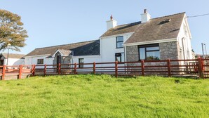 A two-story house with a stone facade and a red wooden fence in front. - Buarthau Cottage (Caernarfon)
