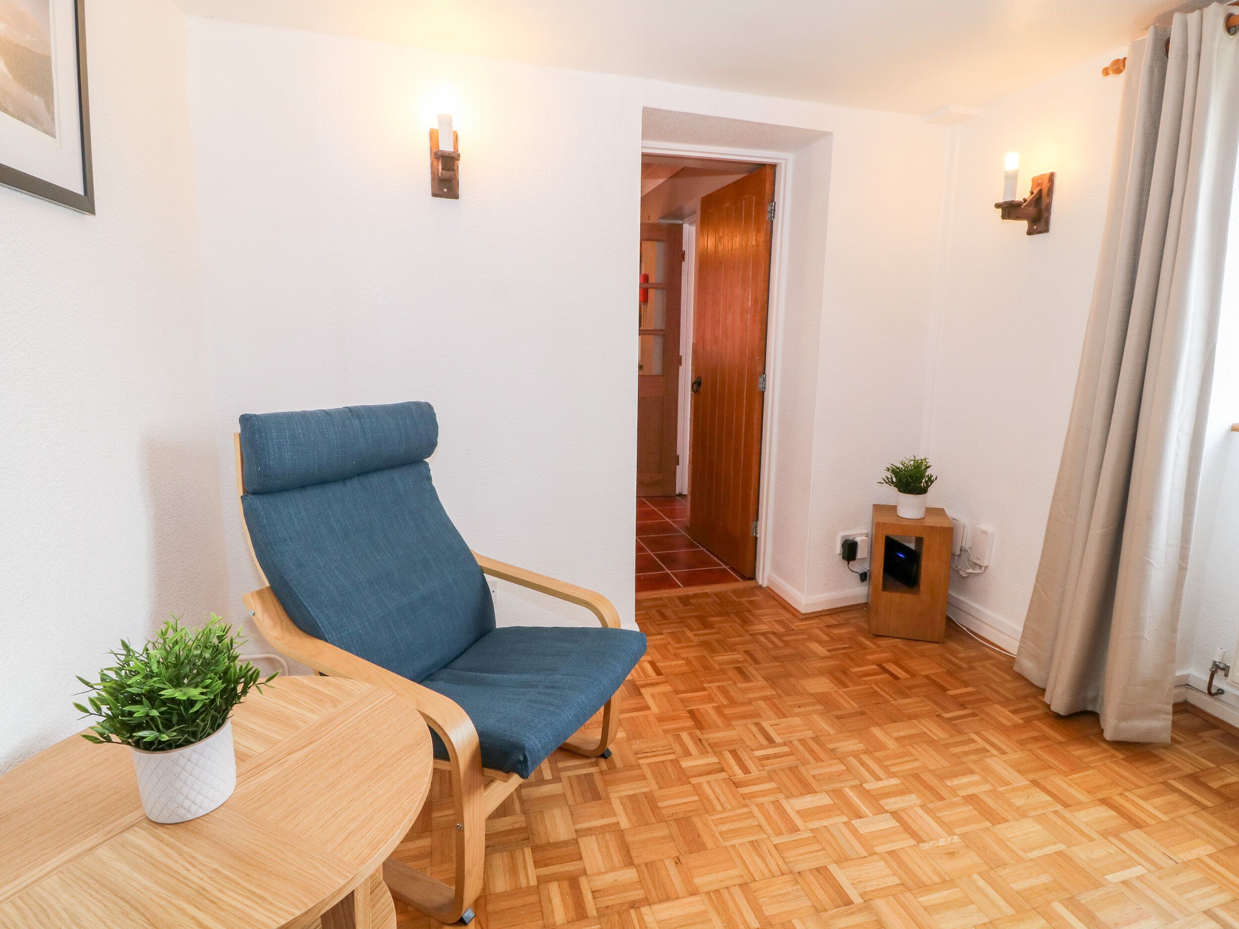 A room with a blue chair, a small table with a plant, and a wooden floor.