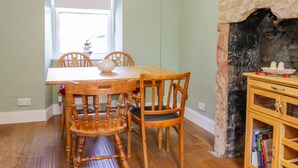 Een eetkamer met een houten tafel en stoelen, een raam en een stenen openhaard.