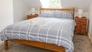 Een slaapkamer met een houten bed, twee nachtkastjes en een raam met uitzicht op bomen.