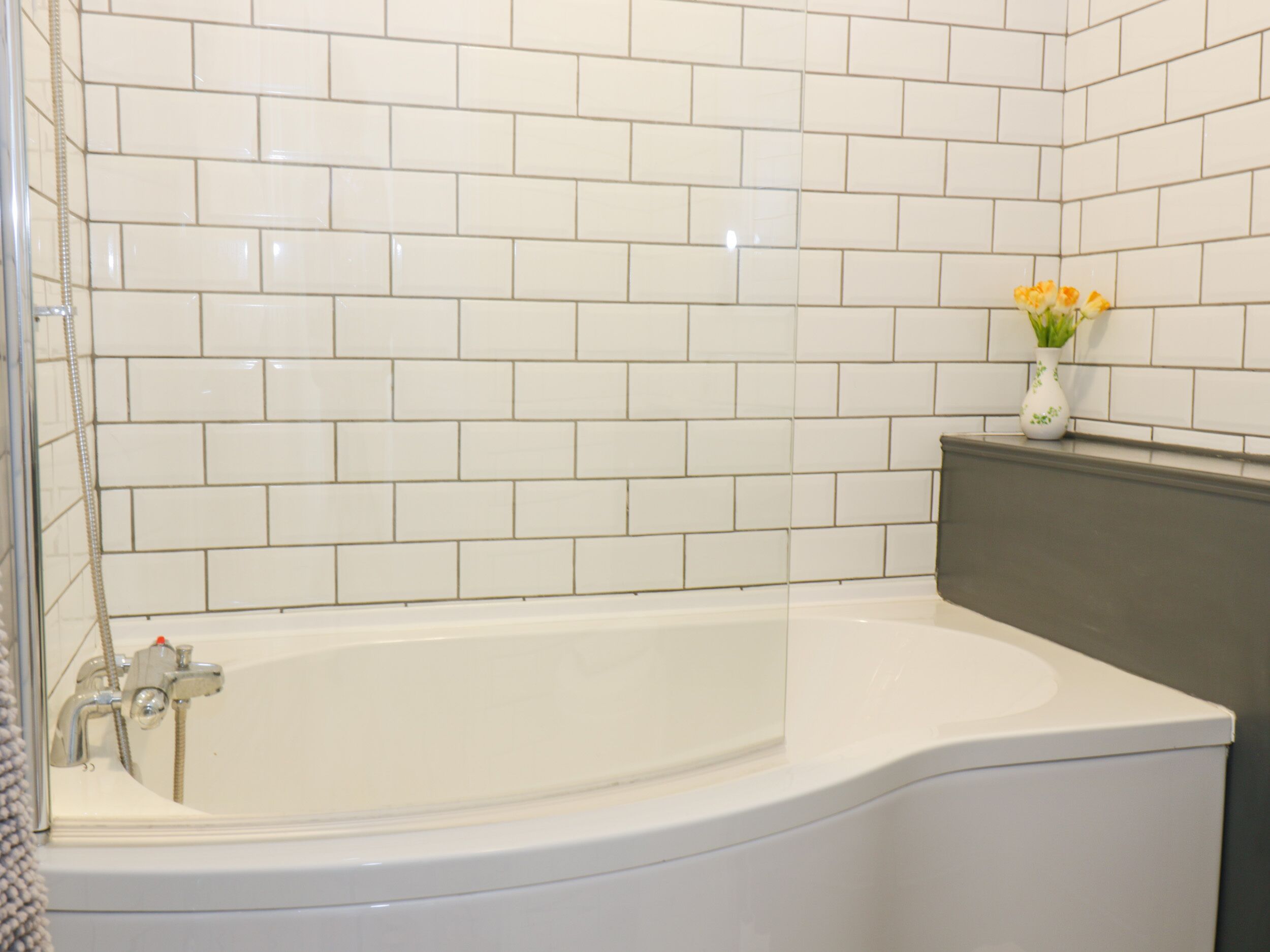 A bathroom with white subway tiles, a white bathtub, and a small vase with flowers on the counter.