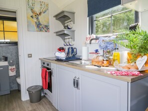 A modern kitchen with white cabinets, a wooden countertop, and a window with a view of greenery. - High Rigg Shepherd's Retreat (Brampton)