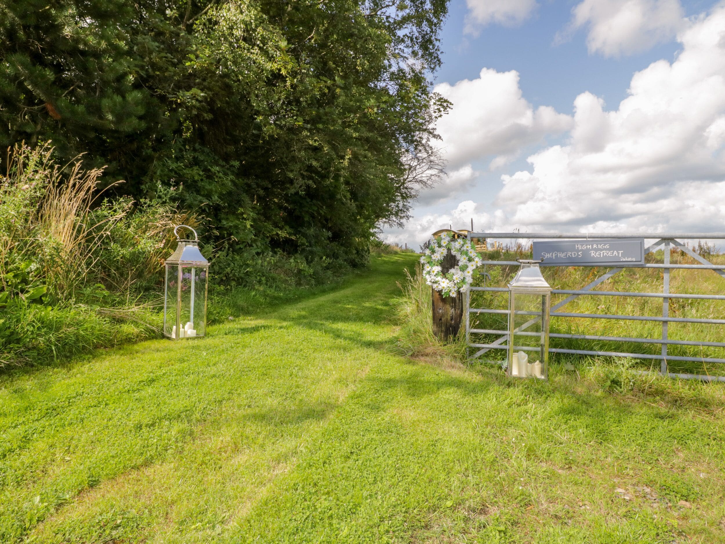 Un sentier rural menant à une porte sur laquelle est apposée une pancarte indiquant « Highrigg Shepherds Retreat ».