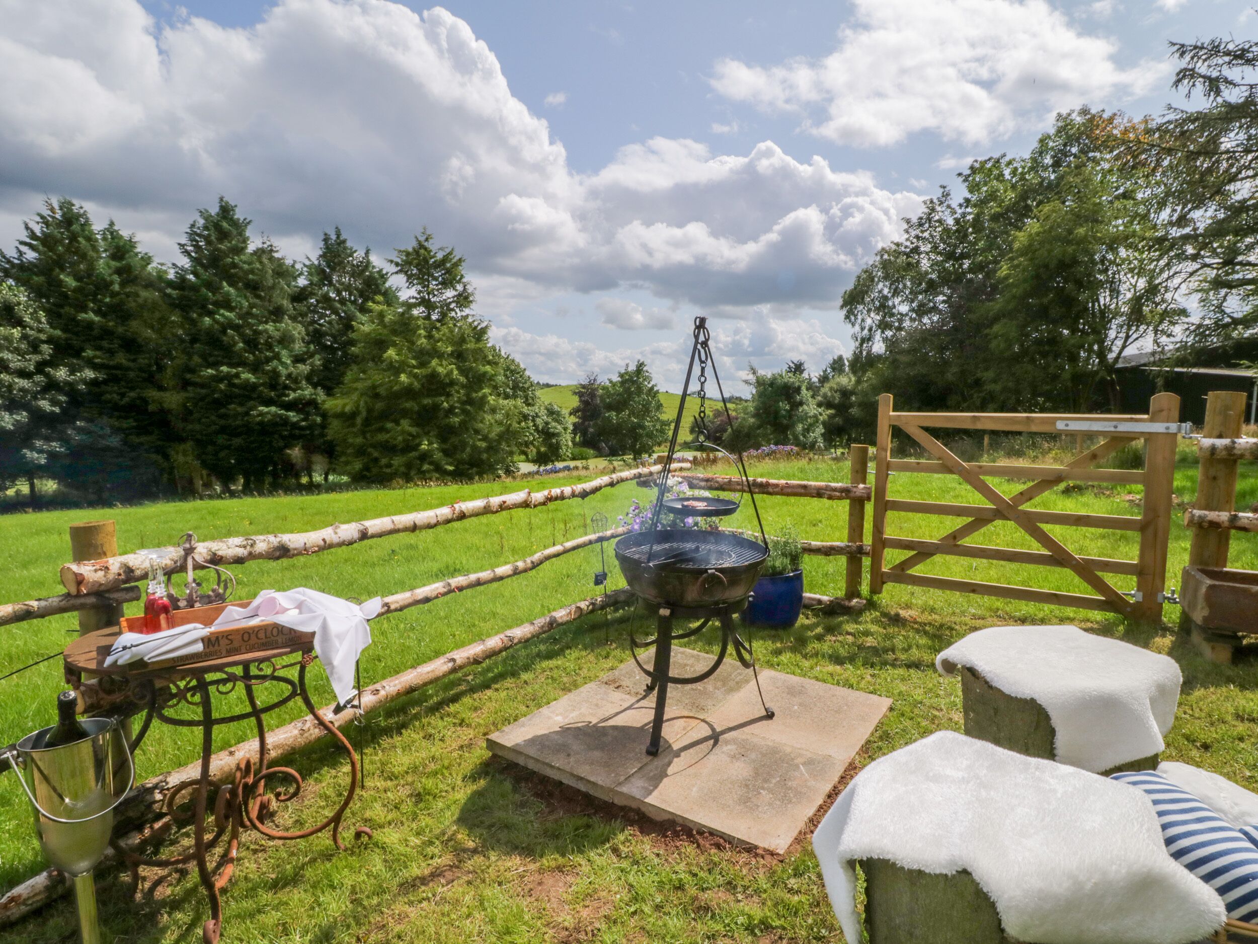An outdoor cooking area with a grill, a wooden table with a cloth, and a gate.