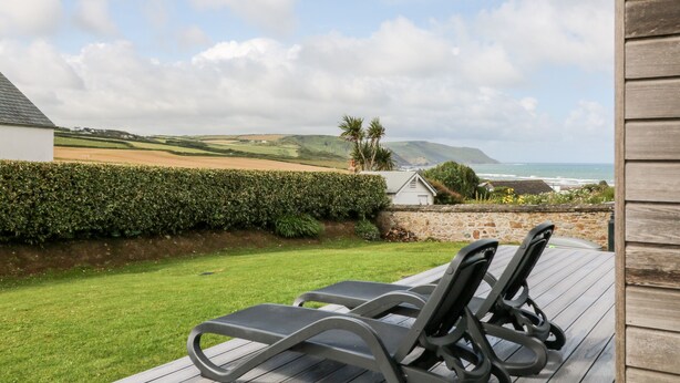 Eine Terrasse mit zwei Liegestühlen mit Blick auf eine Küstenlandschaft mit Hügeln und Meerblick.