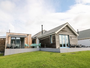 Une maison moderne dotée d’une grande porte vitrée, d’un patio couvert et d’une pelouse bien entretenue.