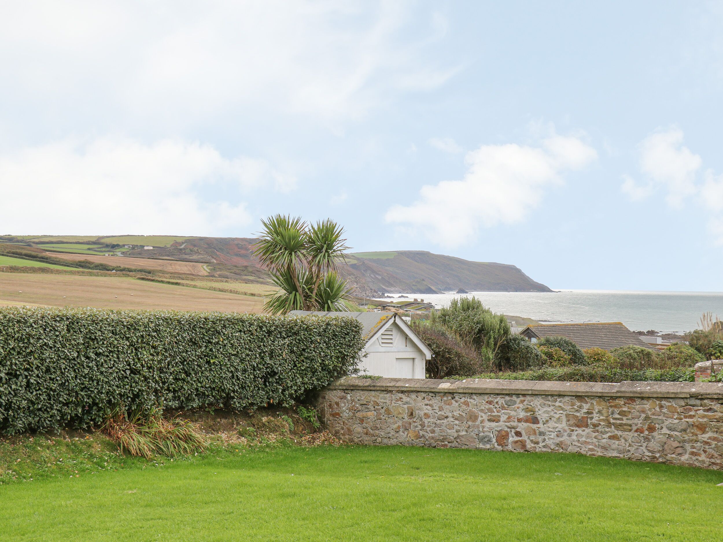A coastal landscape with a stone wall, a small white building, and a view of the sea.
