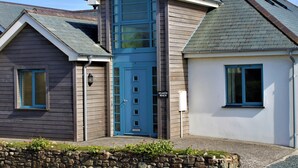 Ein zweistöckiges Haus mit einer blauen Haustür, einer Steinmauer im Vordergrund und einer Steinmauer auf der linken Seite.